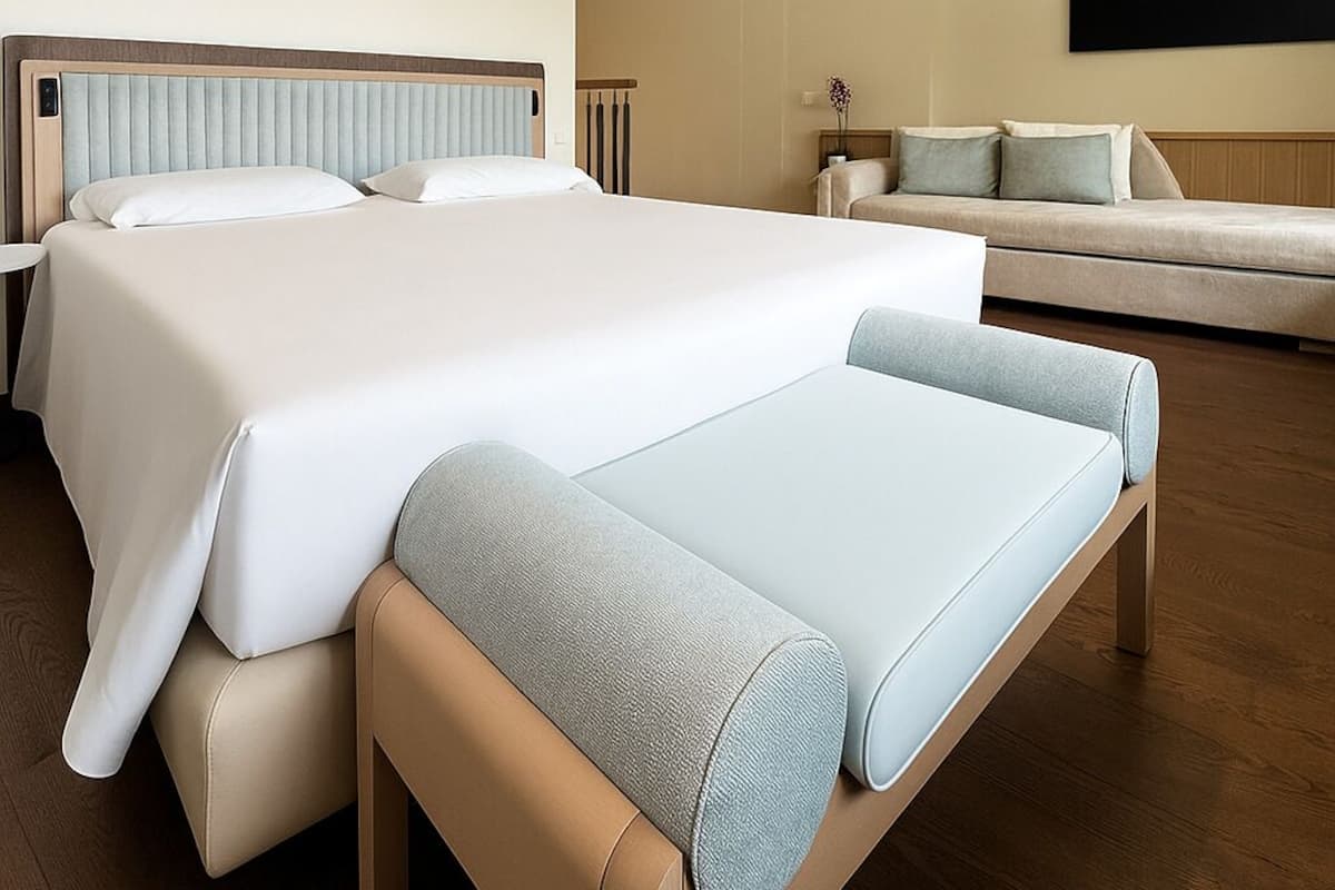 A modern hotel room with two beds, a sofa, and a flat-screen TV on the wall.