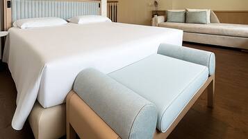 A modern hotel room with two beds, a sofa, and a flat-screen TV on the wall.