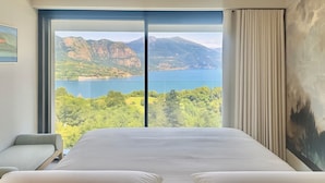 Un dormitorio con una cama grande, una silla y vistas a montañas y un lago.