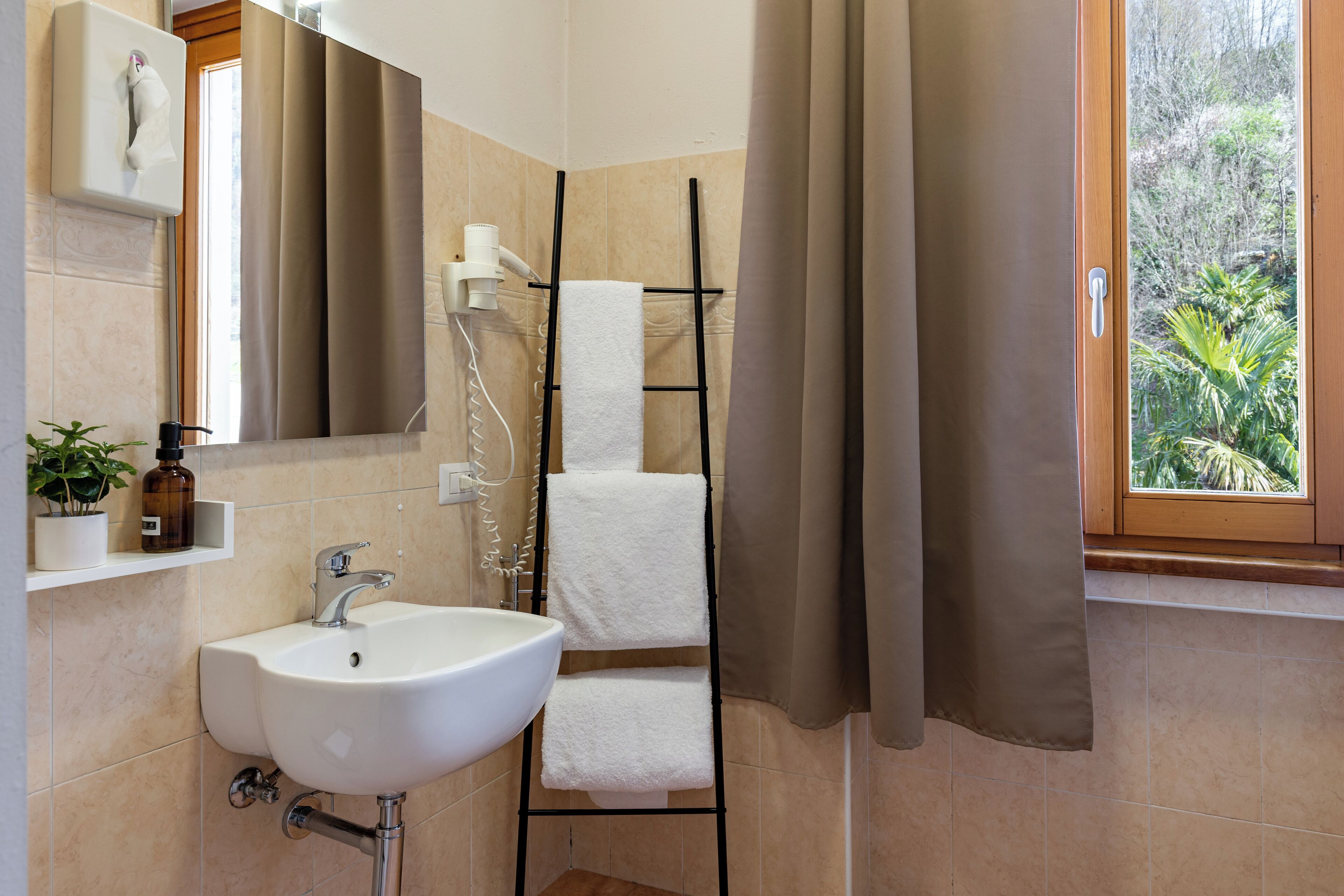 Un baño con un lavamanos blanco, un perchero, una ducha y una ventana con vistas a la vegetación.