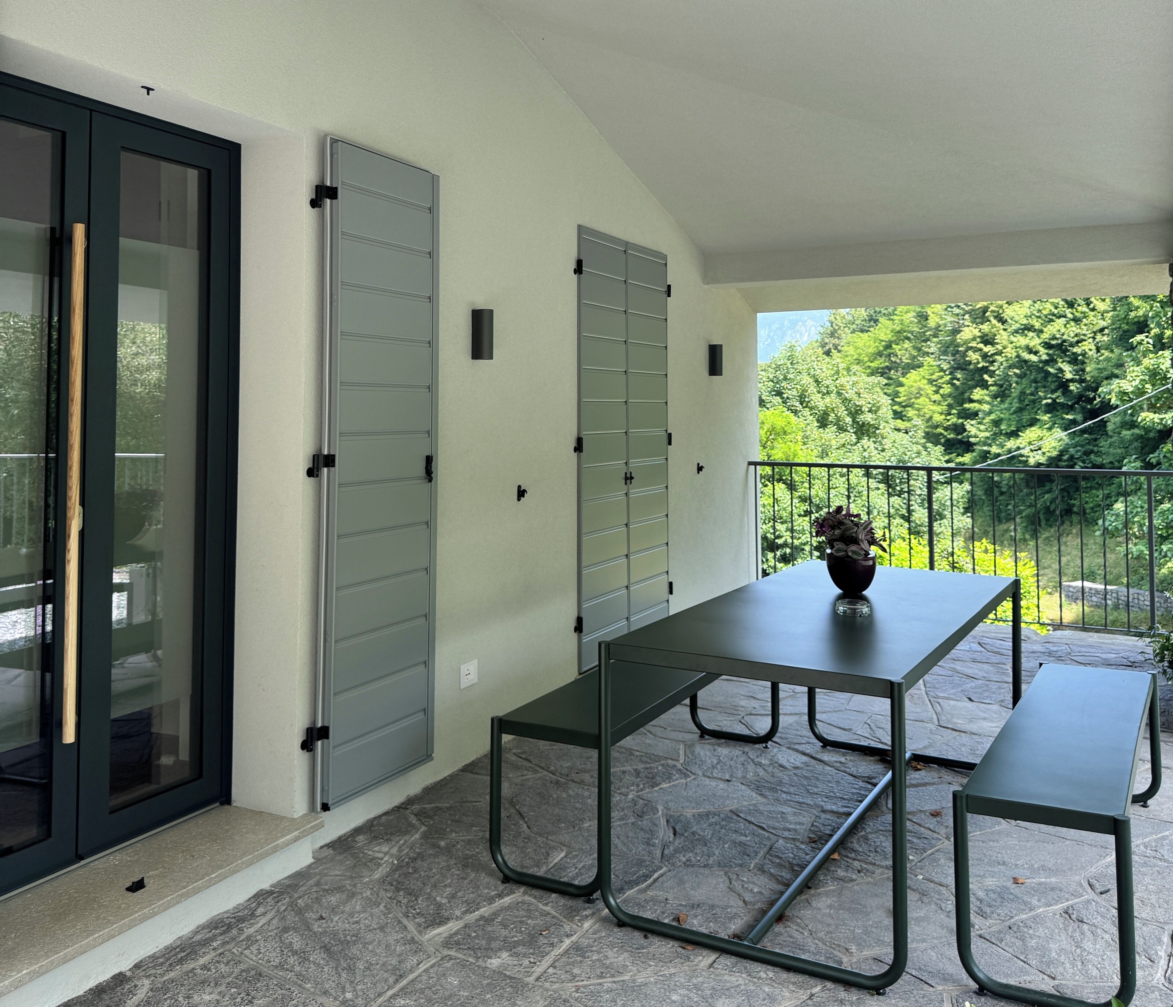 A patio area with a table and benches, a sliding glass door, and a view of greenery.
