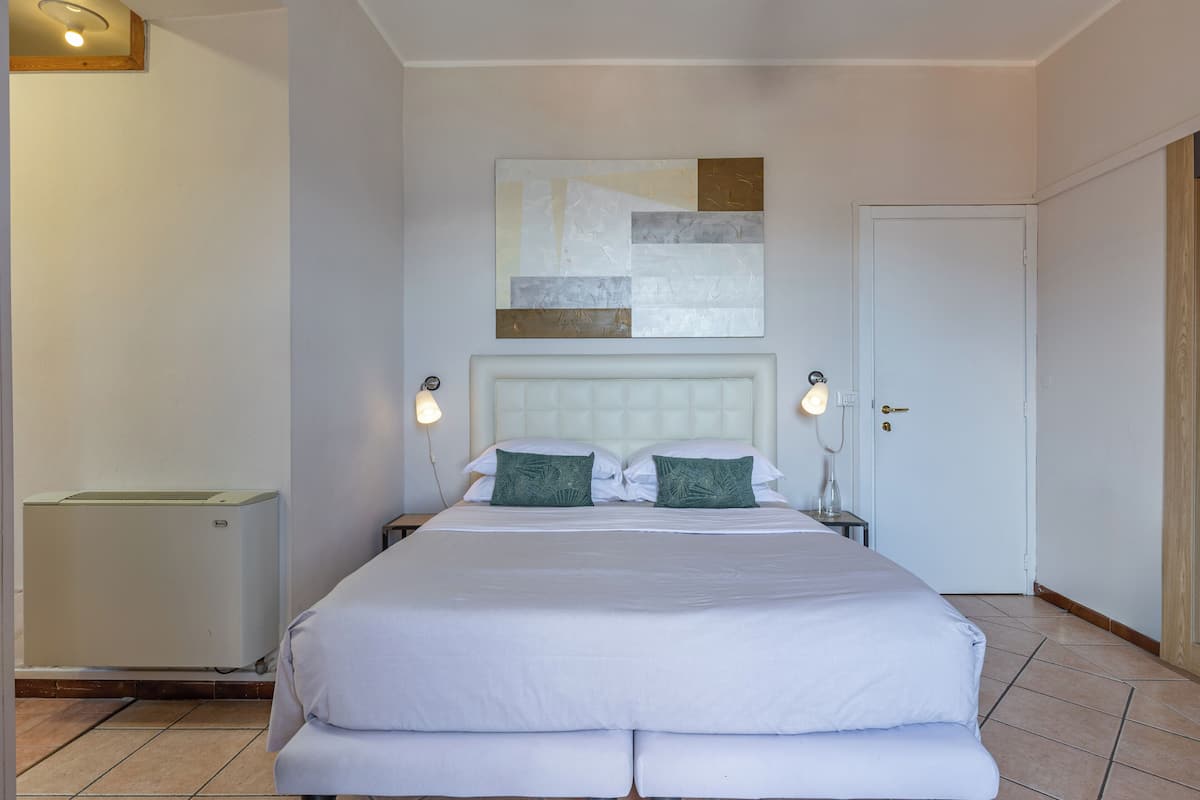 A hotel room with a large bed, two bedside lamps, a wall-mounted abstract art piece, and a door.