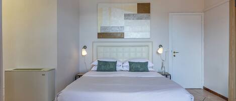 A hotel room with a large bed, two bedside lamps, a wall-mounted abstract art piece, and a door.