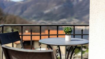 A balcony with a round table and a chair, a potted plant, and a view of mountains.