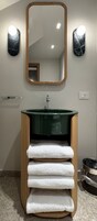 A bathroom with a green sink, wooden towel holder, and a mirror with lights.
