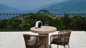 Une terrasse avec une table ronde et deux chaises en osier, offrant une vue sur un paysage montagneux et la mer.