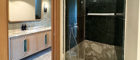 A modern bathroom with a glass-enclosed shower, a marble-tiled floor, and a wooden vanity with a large mirror.