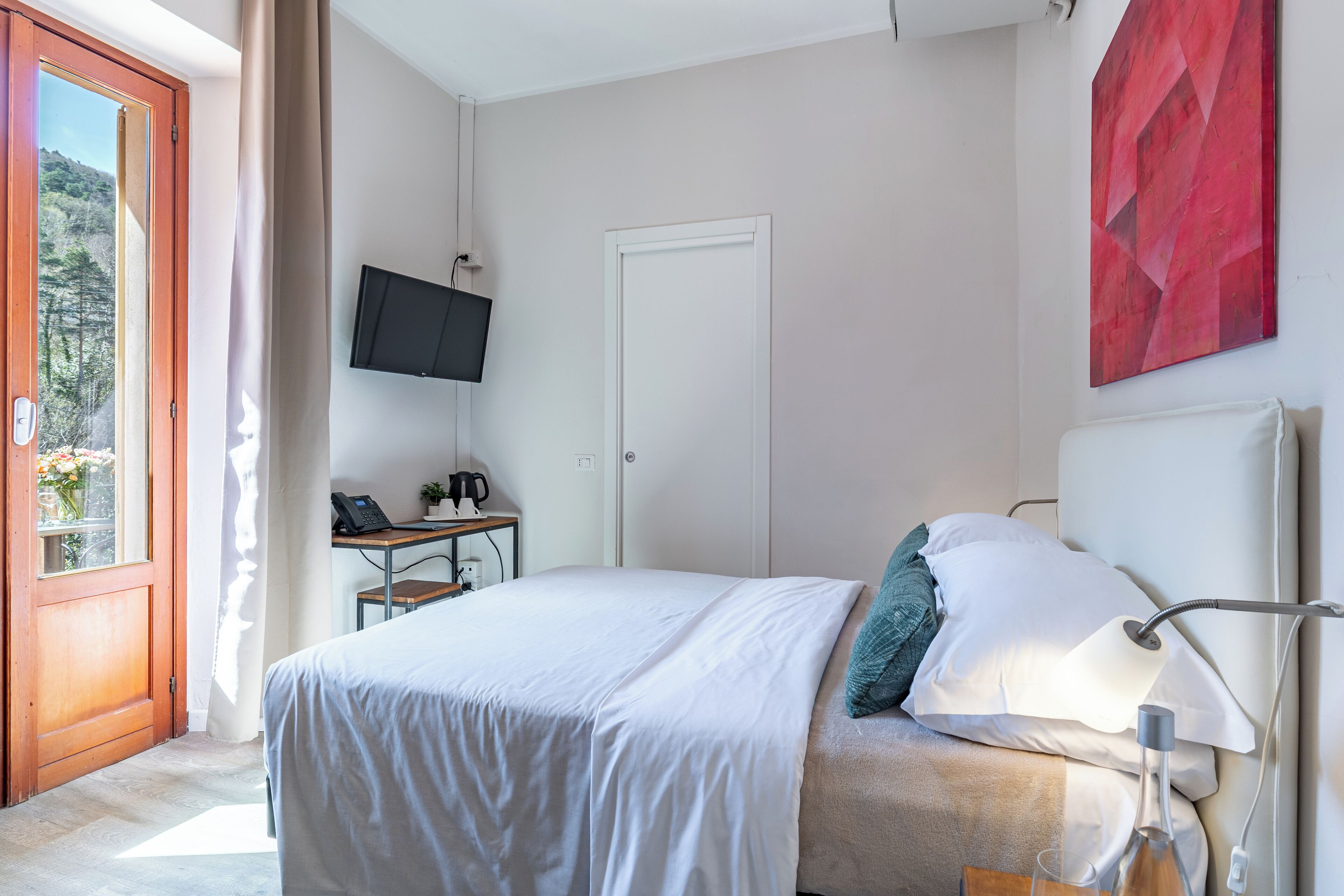 Ein Schlafzimmer mit Bett, Schreibtisch, Fernseher und einem Fenster mit Blick auf Bäume.