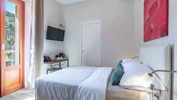Ein Schlafzimmer mit Bett, Schreibtisch, Fernseher und einem Fenster mit Blick auf Bäume.