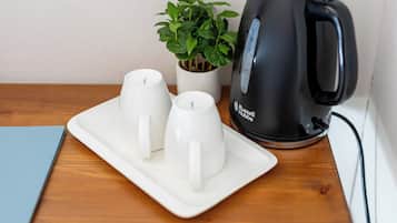 A table with a white plate holding two white cups, a black kettle, and a potted plant.