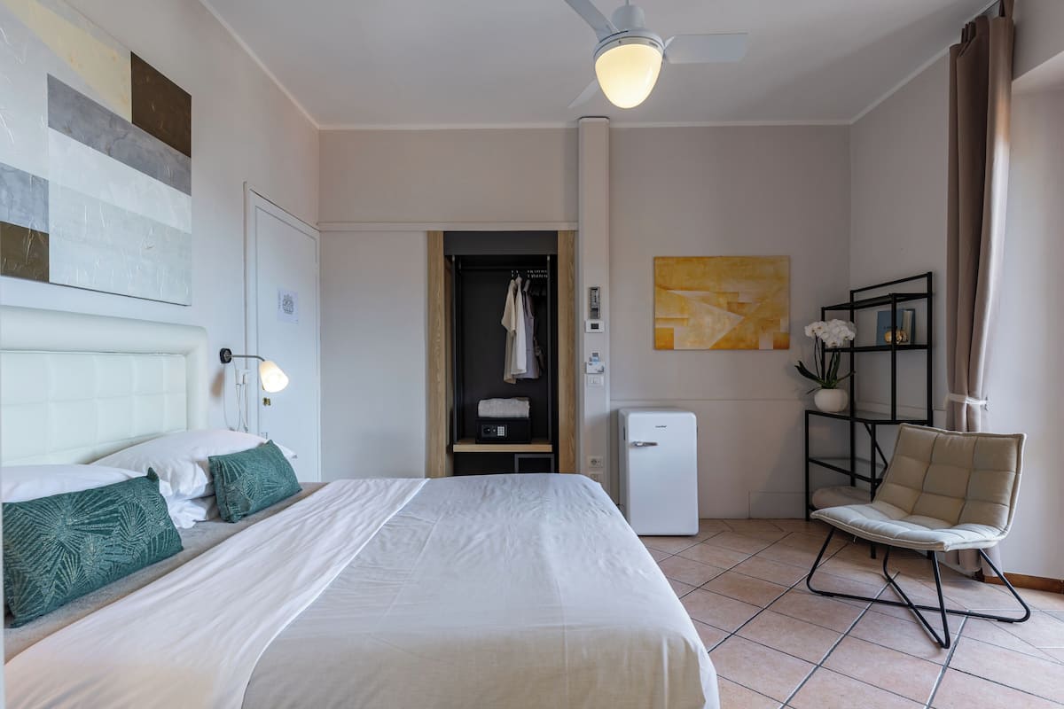 A hotel room with a bed, a chair, a wardrobe, a desk, and a ceiling fan.