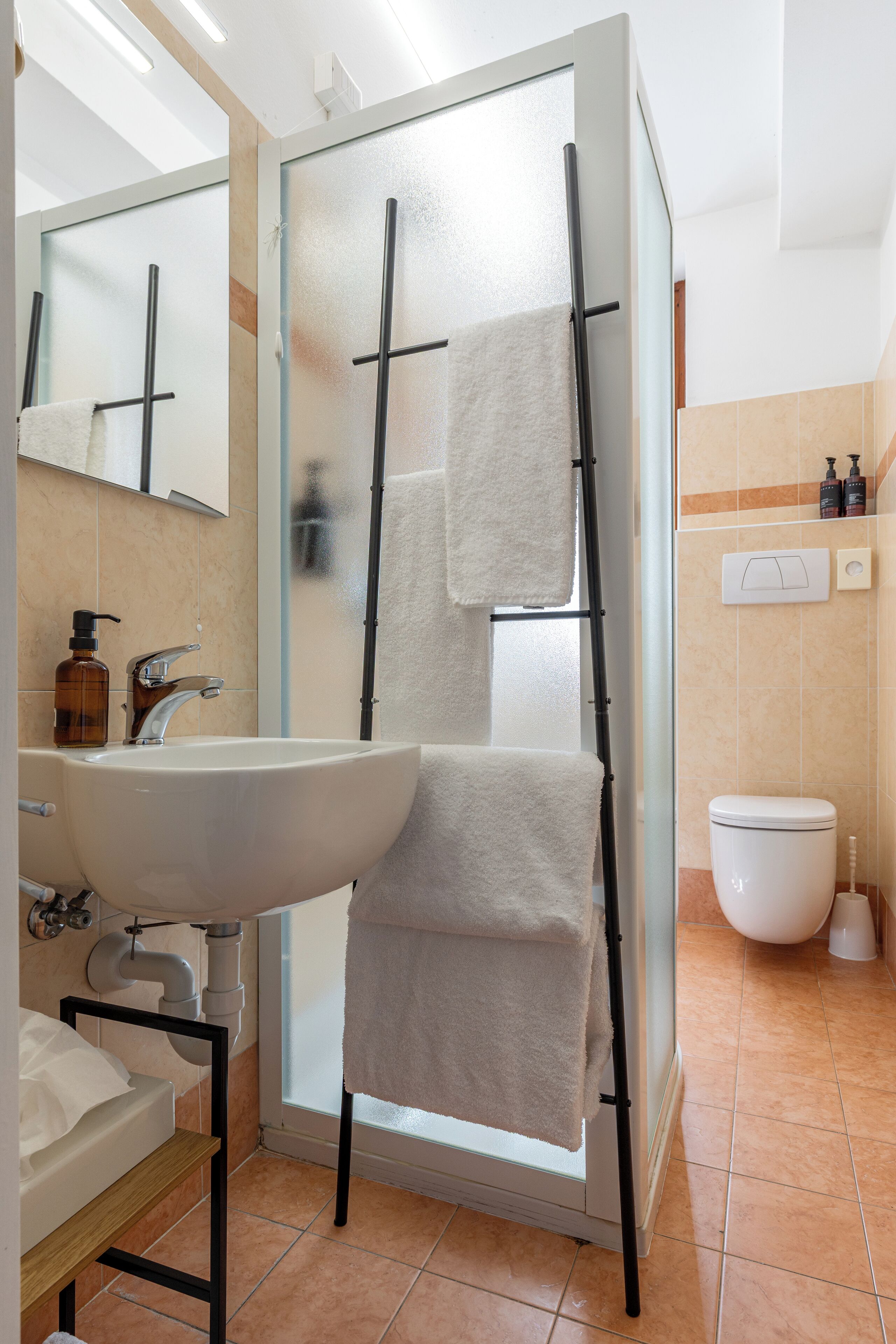 A bathroom with a white sink, a mirror, a towel rack, a toilet, and a shower with a glass door.