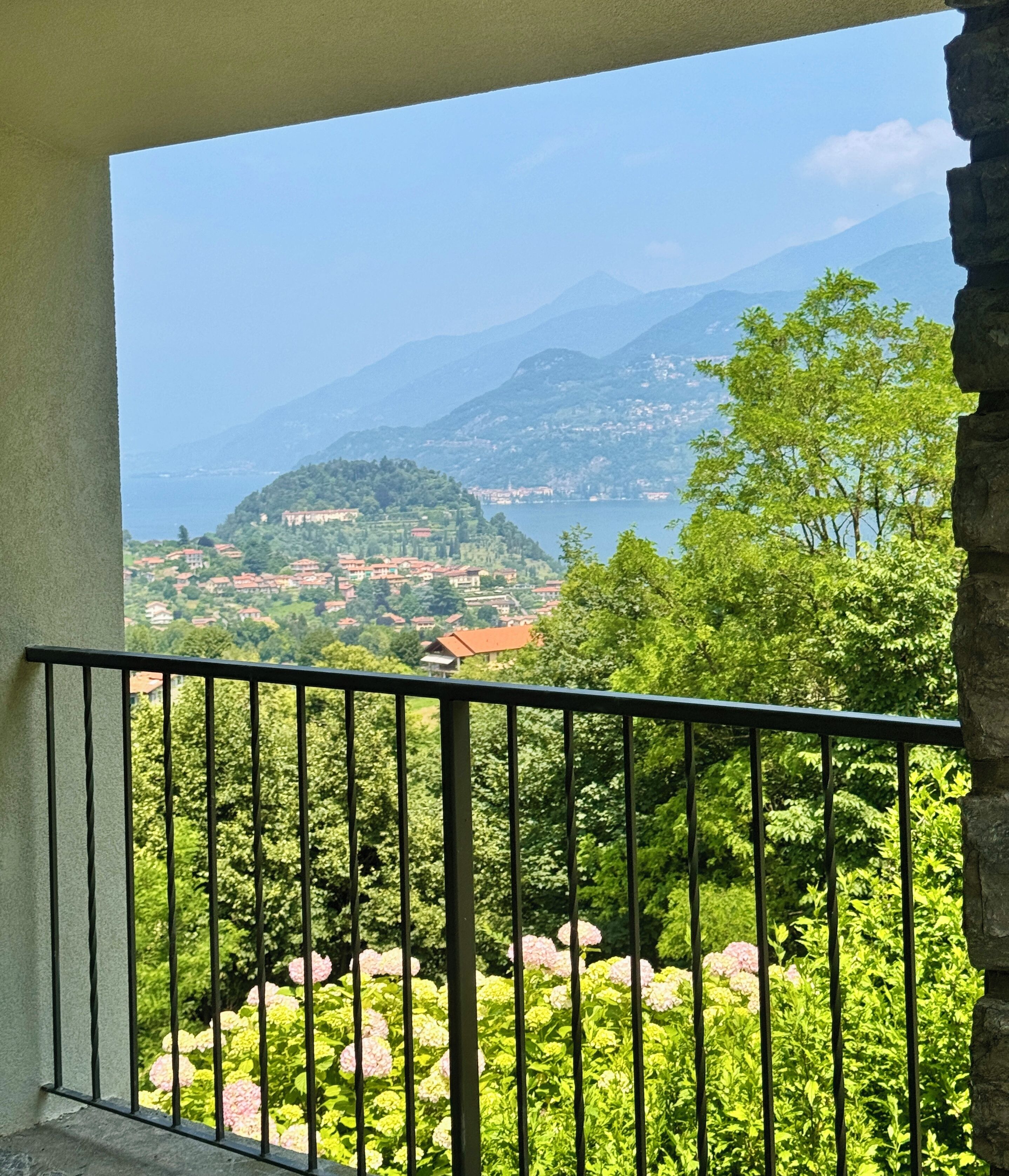 A balcony with a view of a mountainous landscape, lush greenery, and a distant village.