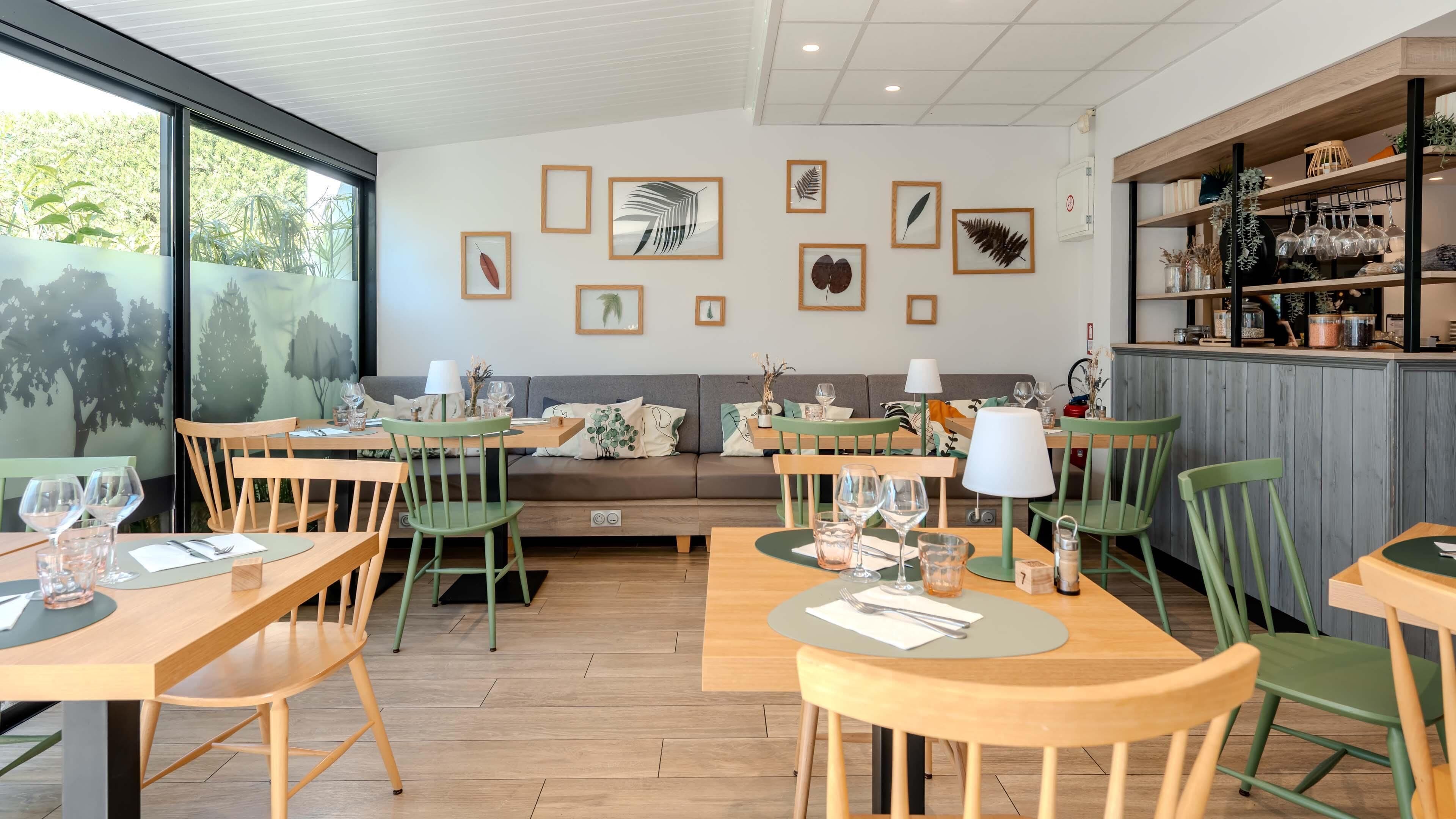 A restaurant with wooden tables and chairs, a sofa, and framed leaf artwork on the wall.
