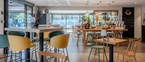 A modern cafe interior with wooden tables and chairs, a blackboard menu, and large windows offering a view of the outdoors.