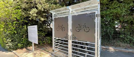 A metal gate with bicycle symbols, a sign listing access rules, and a pathway leading to a forested area.
