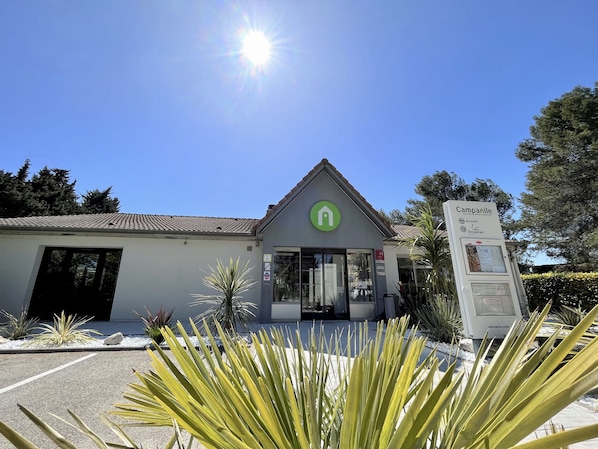 A hotel with a green logo, a signboard, and a clear blue sky. - Campanile NATURE - Orange (Orange)
