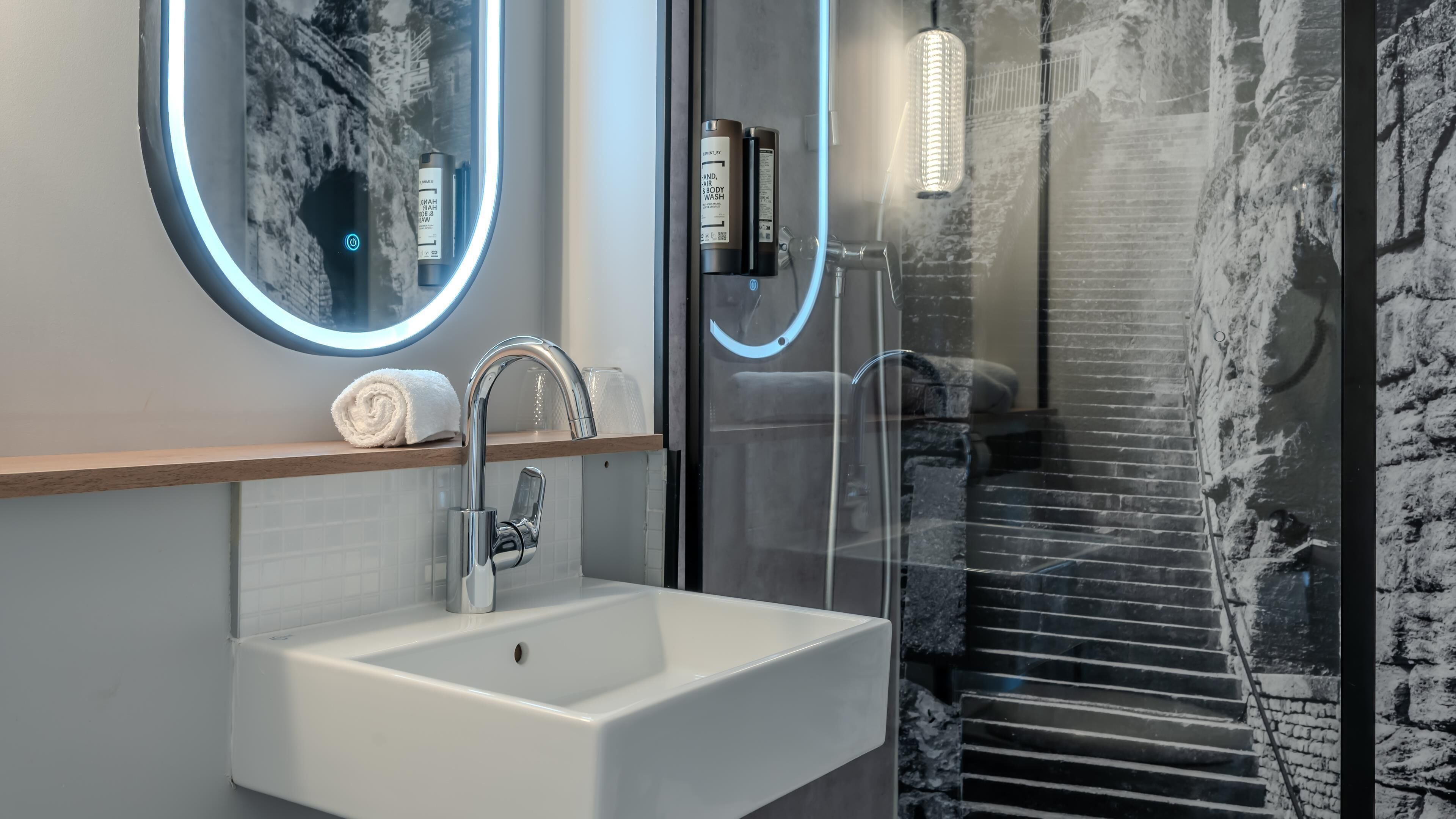 Un baño moderno con un lavabo blanco, un espejo con marco circular y una cabina de ducha de vidrio.