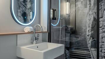 Un baño moderno con un lavabo blanco, un espejo con marco circular y una cabina de ducha de vidrio.