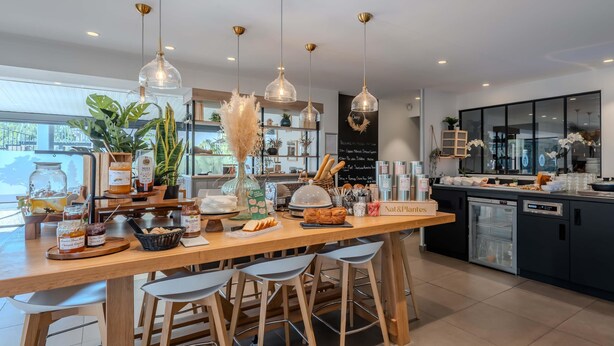 A modern kitchen with wooden bar stools, hanging pendant lights, and a variety of food items displayed on the counter. - Campanile NATURE - Orange (Orange)