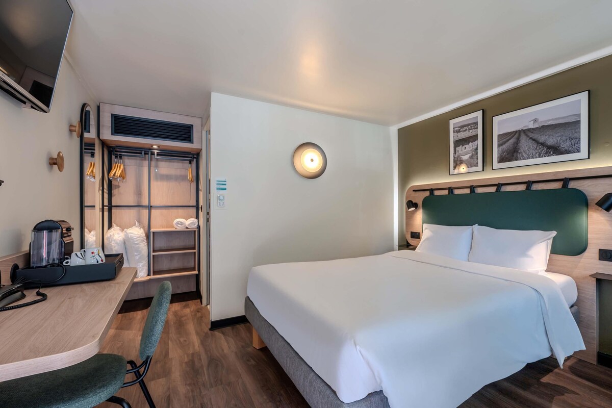 A hotel room with a bed, desk, chair, and a wardrobe.