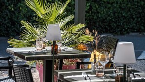 An outdoor dining area with tables set for two, each with a white table lamp, clear glasses, and cutlery. - Campanile NATURE - Orange (Orange)