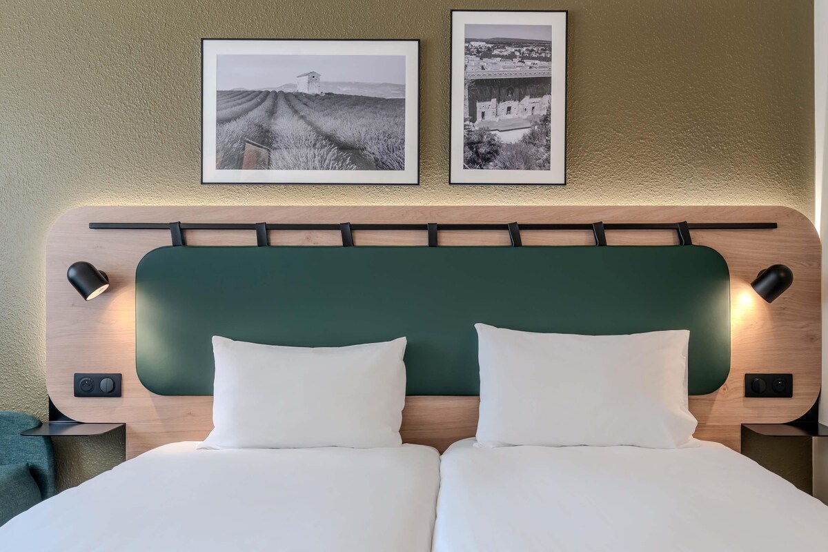 A bed with two pillows, a wooden headboard, bedside lamps, and two framed pictures on the wall.