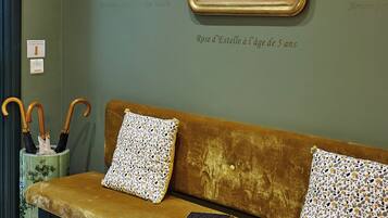 A room with a green wall, a framed portrait, a bench with patterned cushions, and a small table with a book.