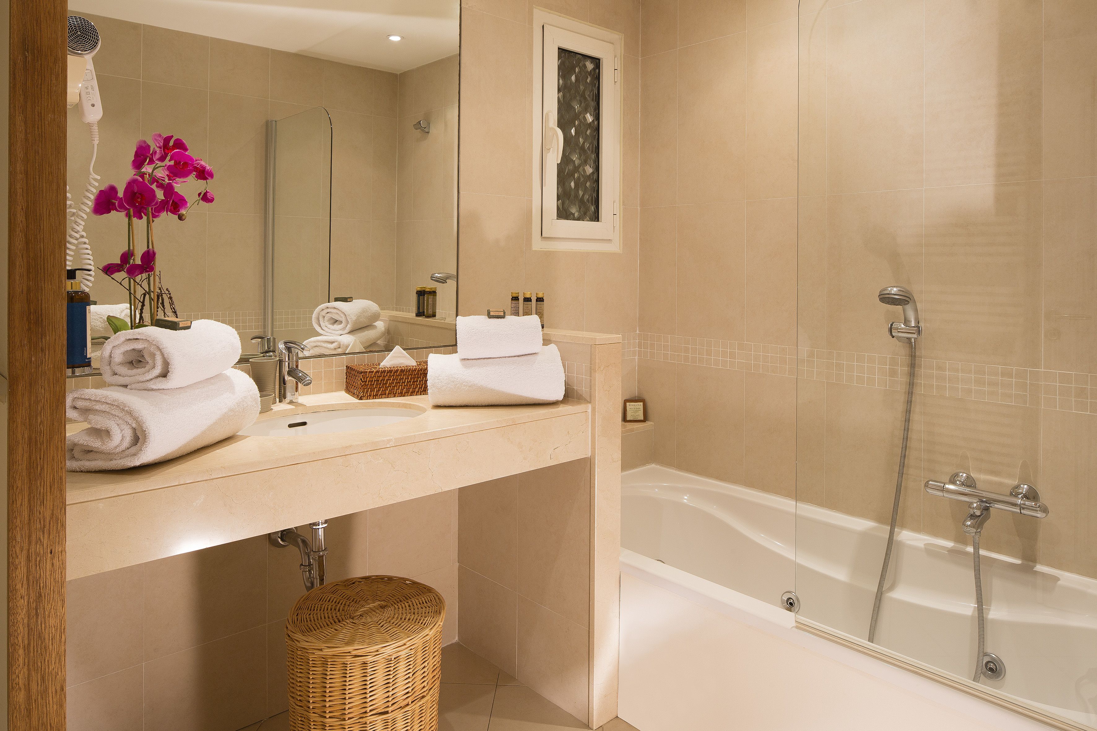A bathroom with a bathtub, a sink, and a mirror. There are towels and a wicker basket.
