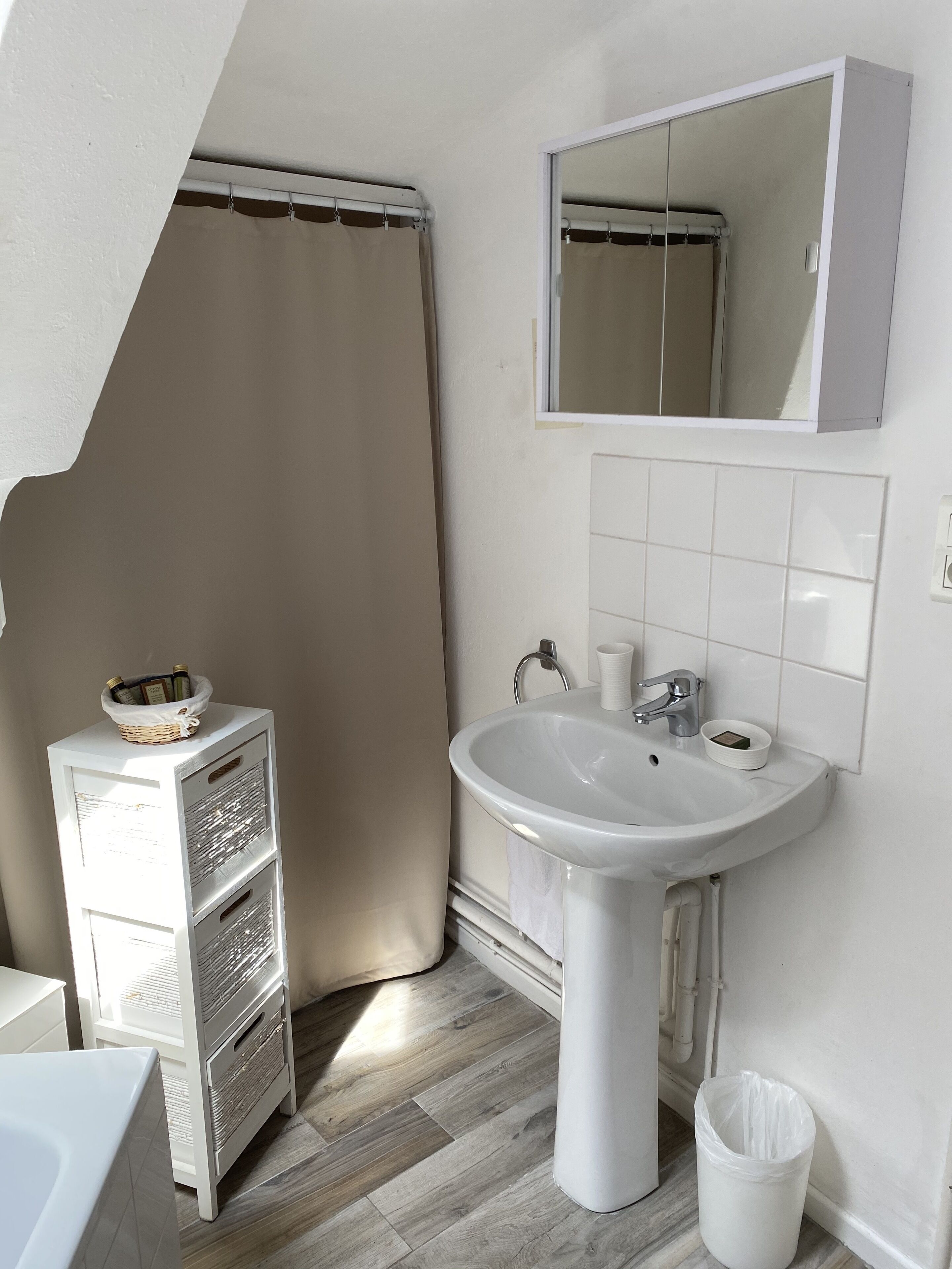 A bathroom with a white sink, a mirror, a shower curtain, and a small shelf with toiletries.