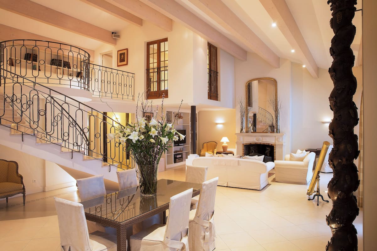 A spacious living area with a staircase, a fireplace, and a dining table with chairs.