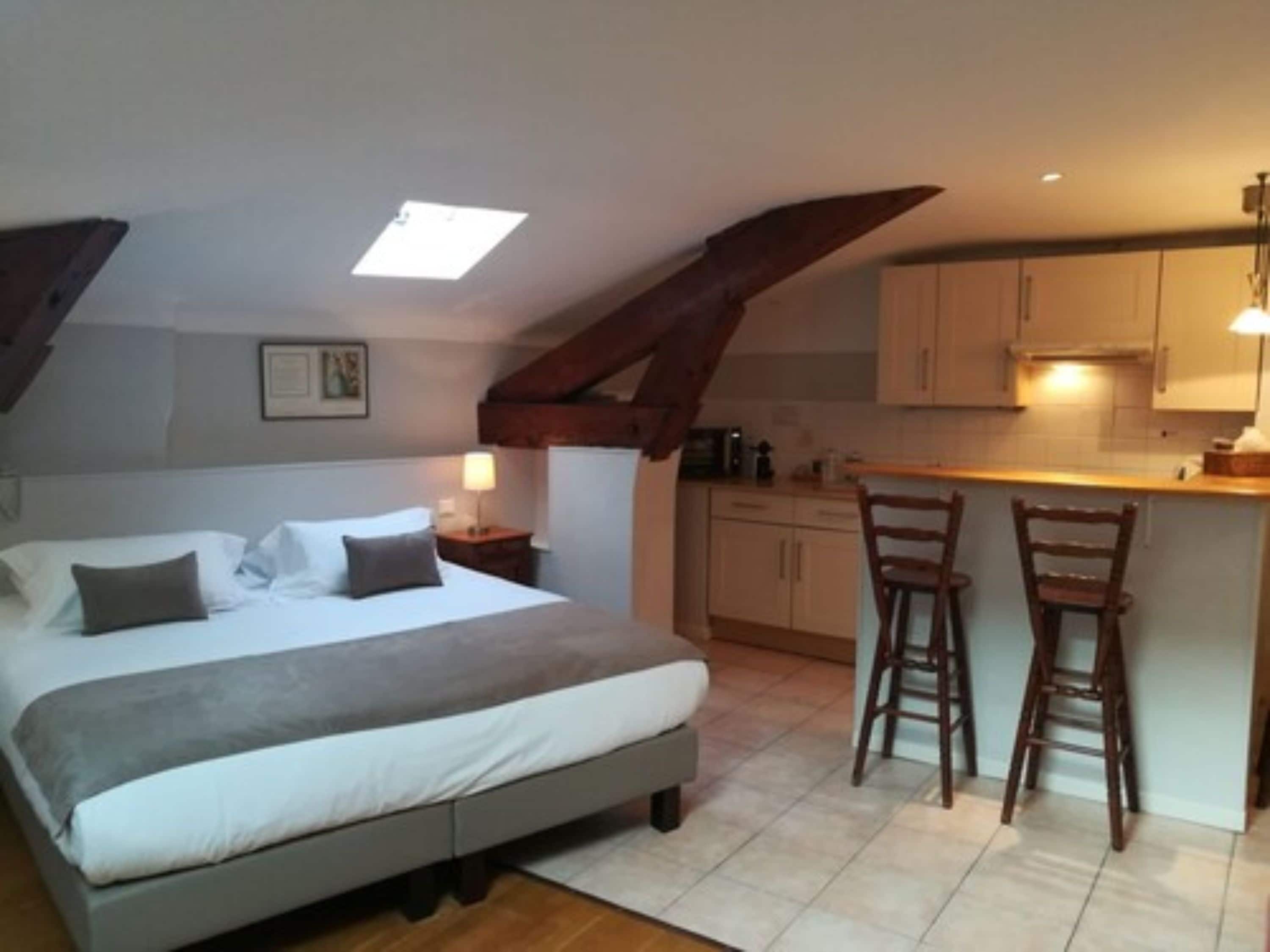 A bedroom with a bed, bedside table, and a small kitchenette with a bar stool.