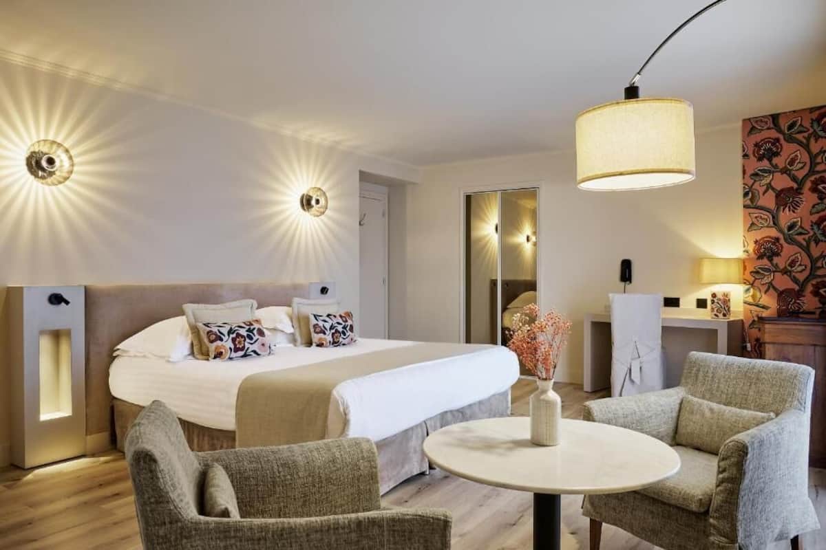 A hotel room with a large bed, two bedside lamps, a round table, and two armchairs.