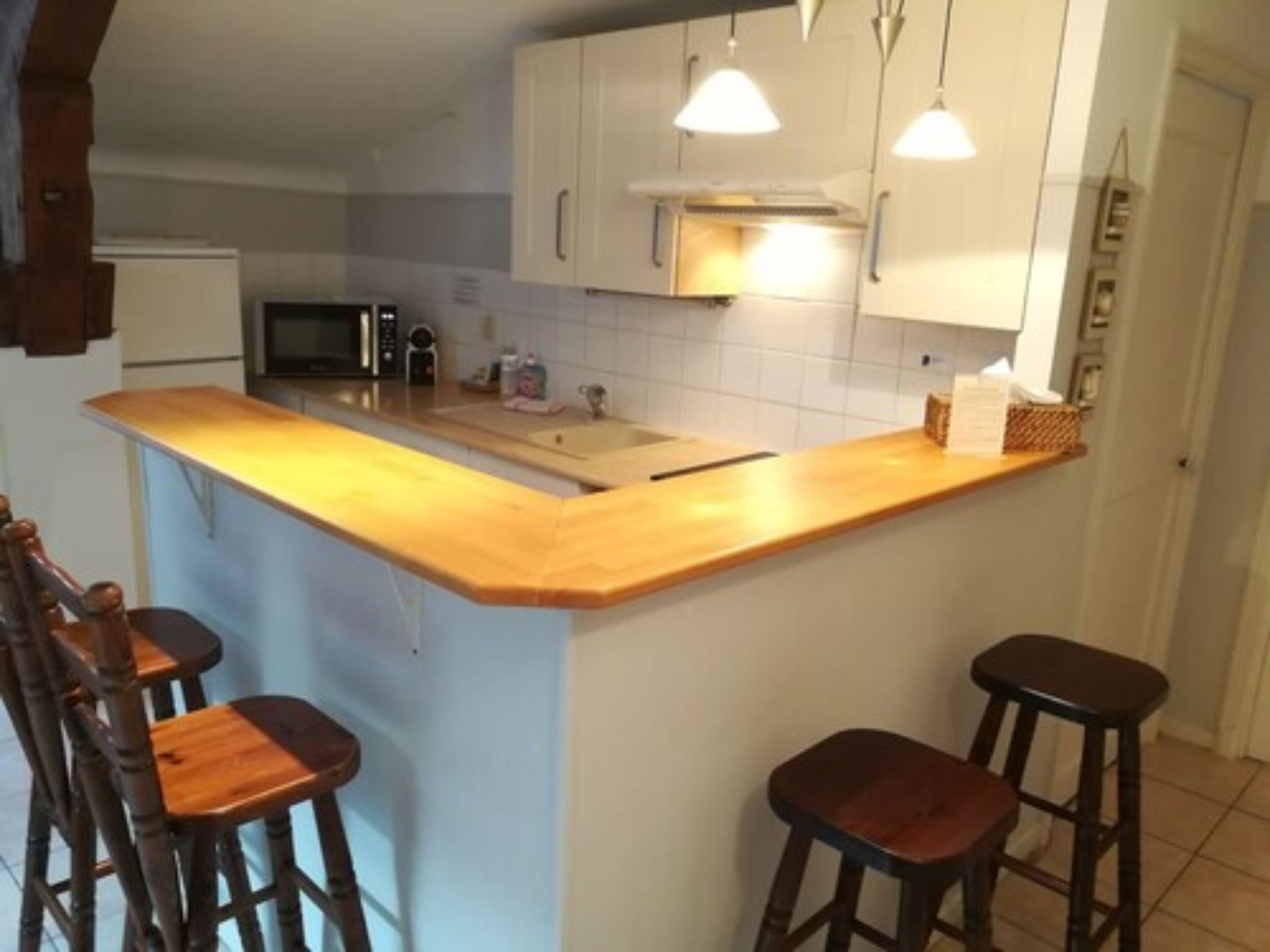 A kitchen with a wooden countertop, white cabinets, a microwave, and two bar stools.