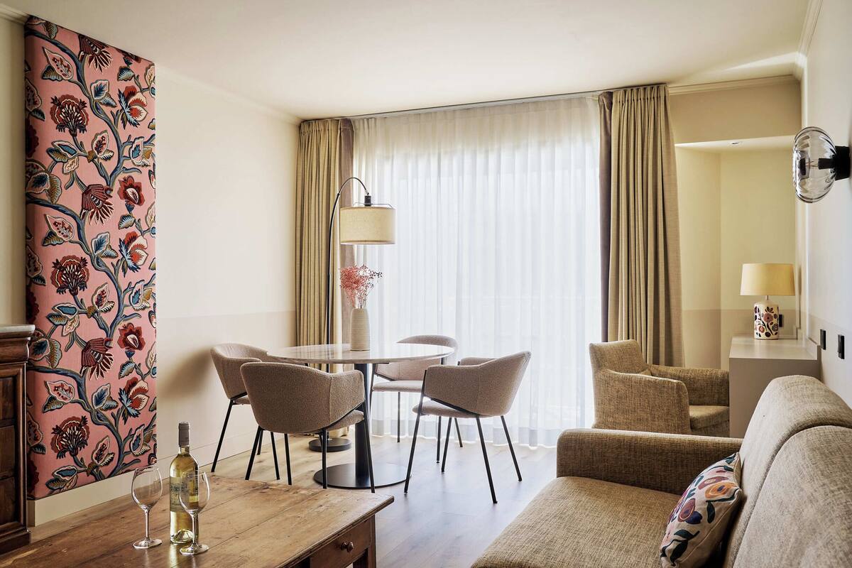 A hotel room with a dining area, a sofa, and a table with wine glasses.