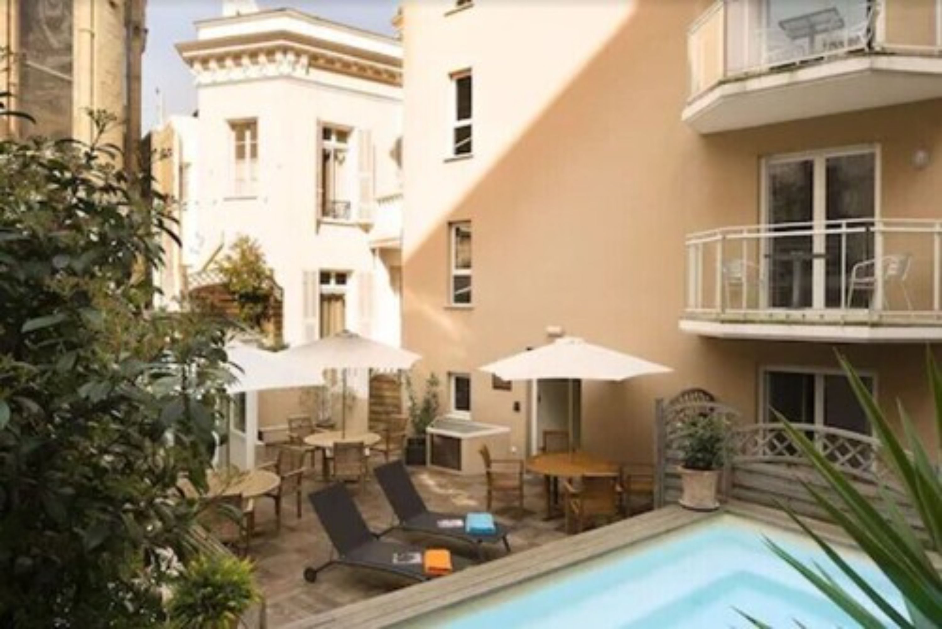 A poolside area with lounge chairs and umbrellas, surrounded by buildings.
