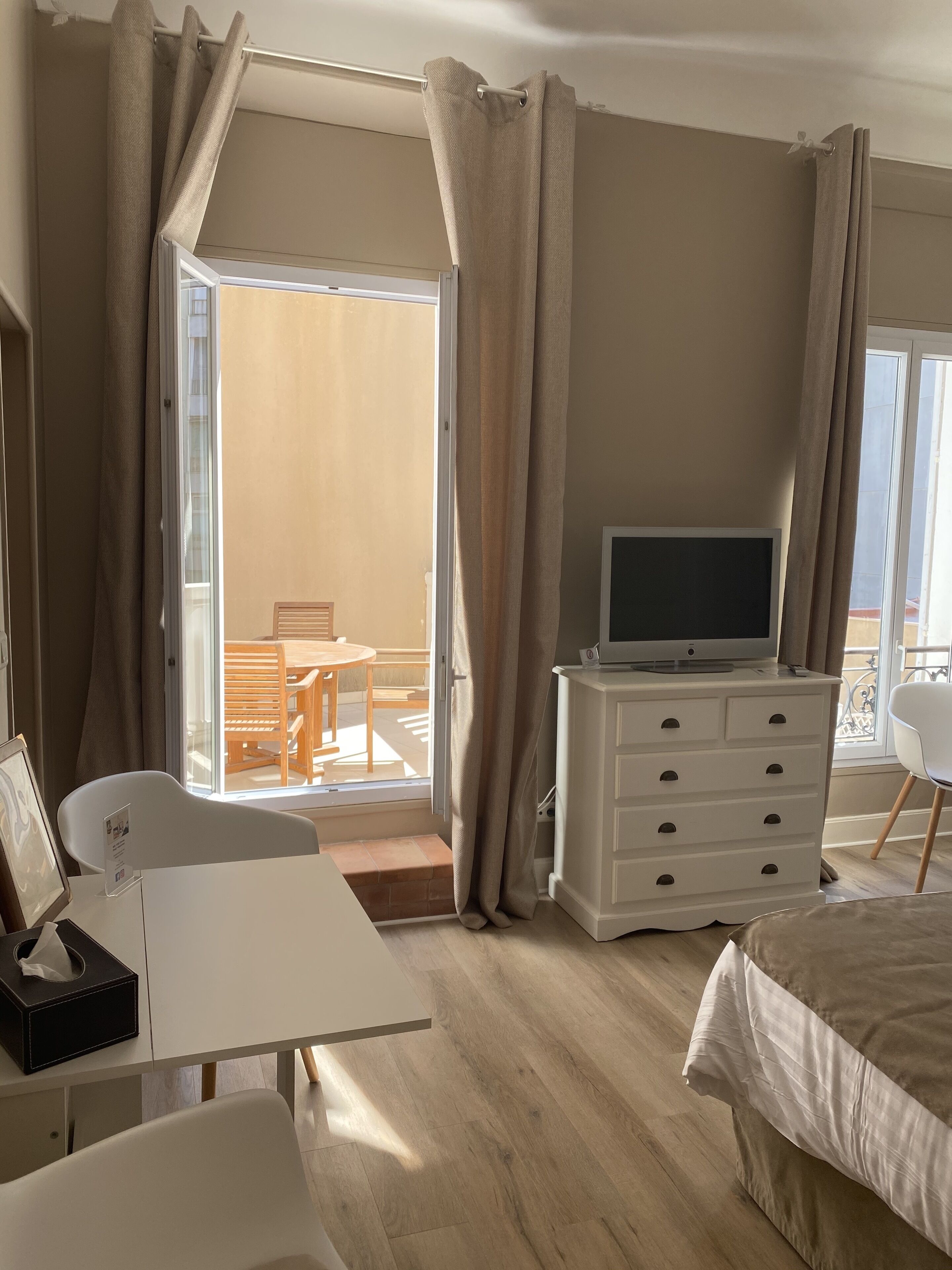 Une chambre d’hôtel avec un lit, un téléviseur posé sur une commode, un bureau avec une chaise et une vue sur le balcon extérieur.