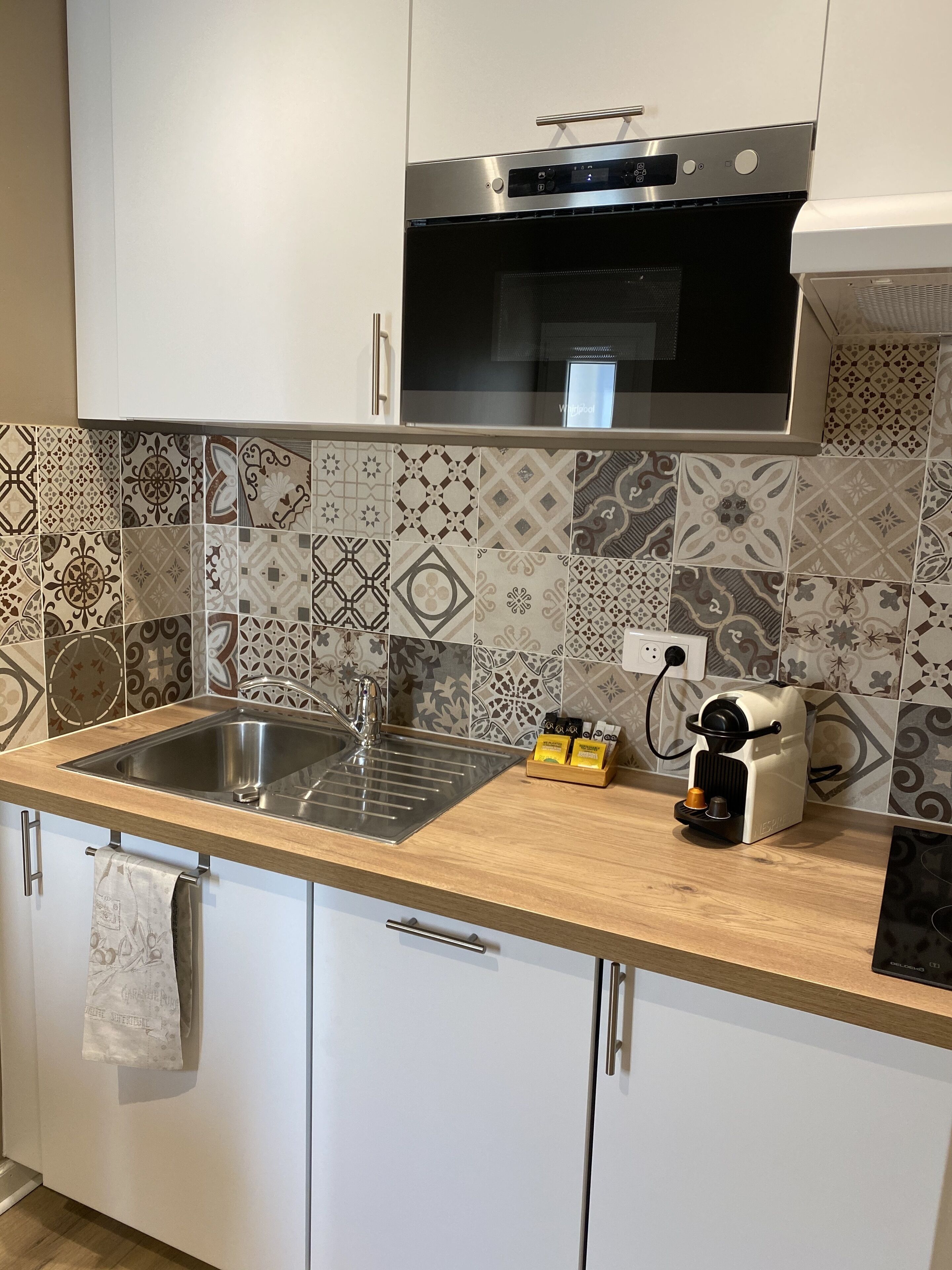 A kitchen with a stainless steel sink, a coffee machine, and patterned tiles.