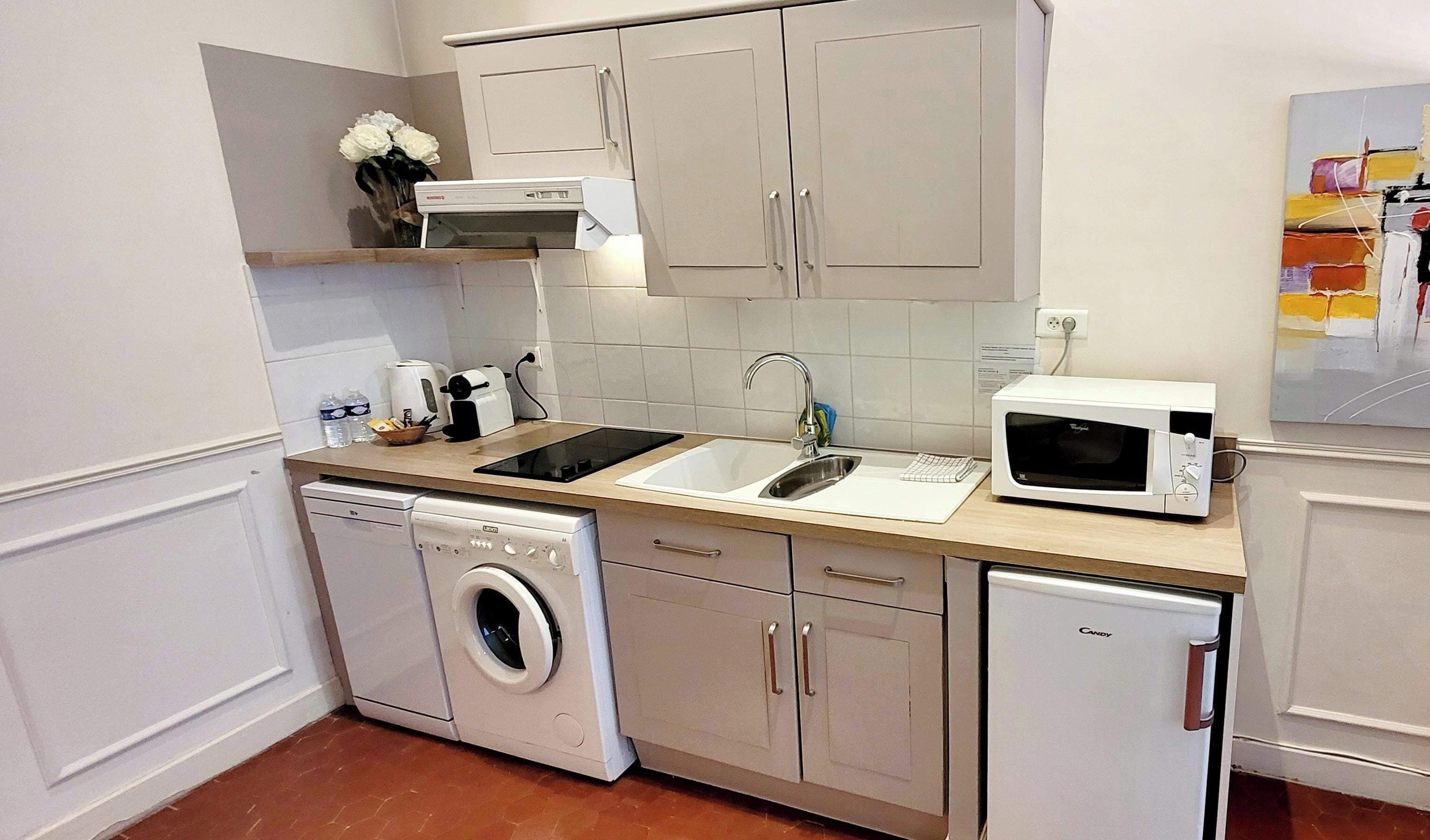 Uma cozinha compacta com máquina de lavar, micro-ondas, pia e torradeira.