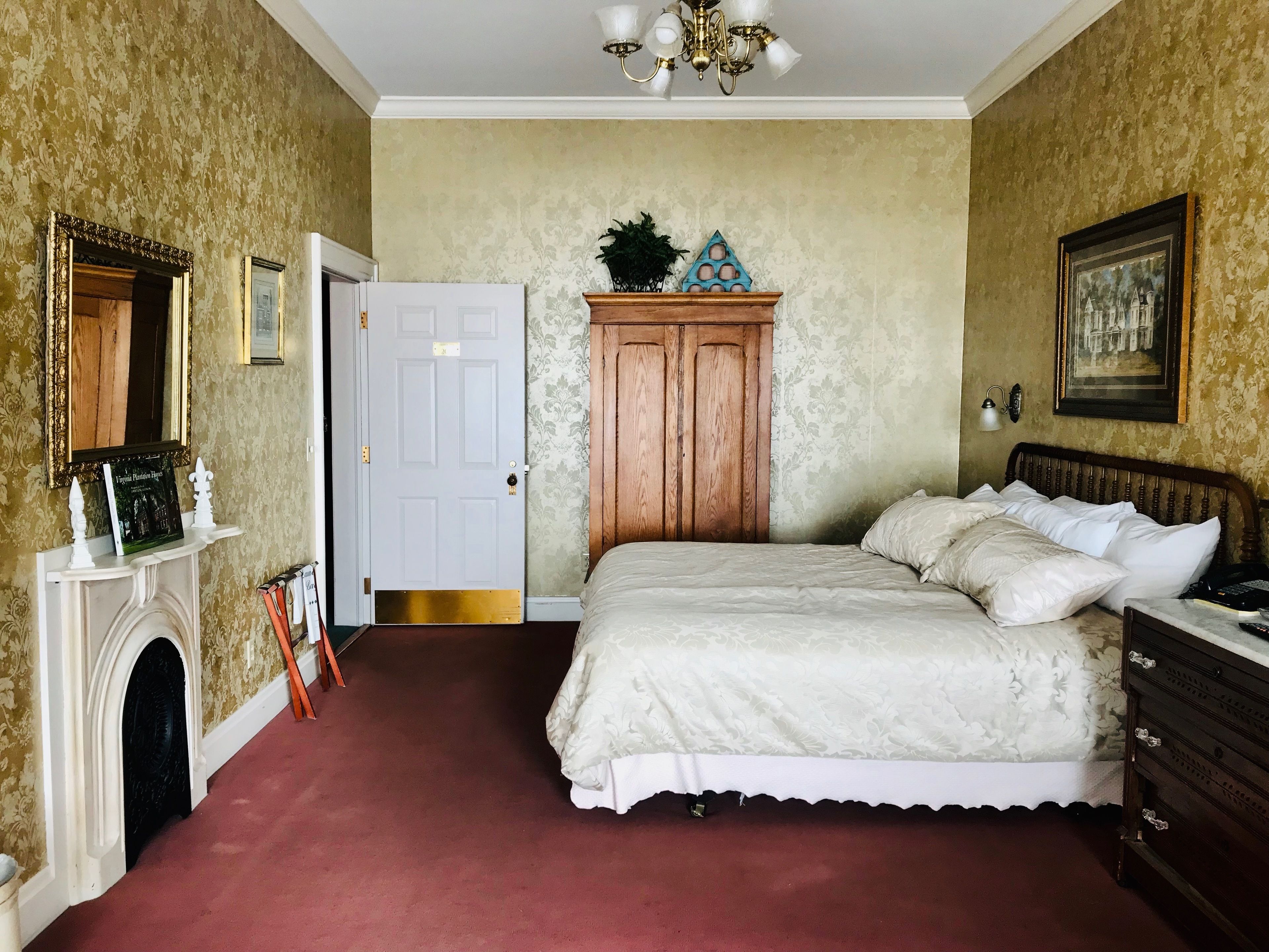 A bedroom with a large bed, a wooden wardrobe, a fireplace, and a chandelier.