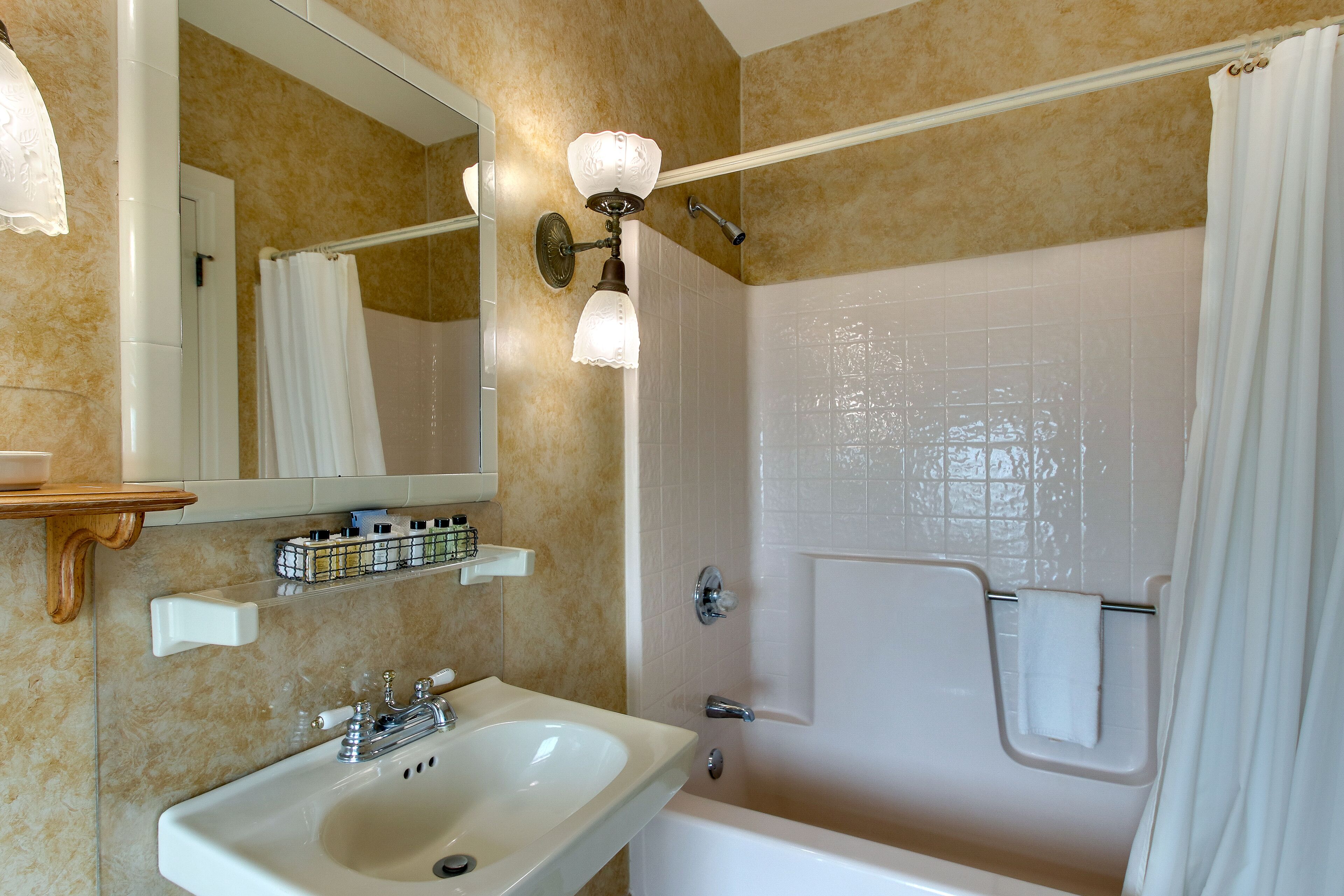 A bathroom with a sink, mirror, shower, and a towel rack.