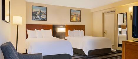 A hotel room with two beds, a desk, a chair, a TV, and artwork on the walls.