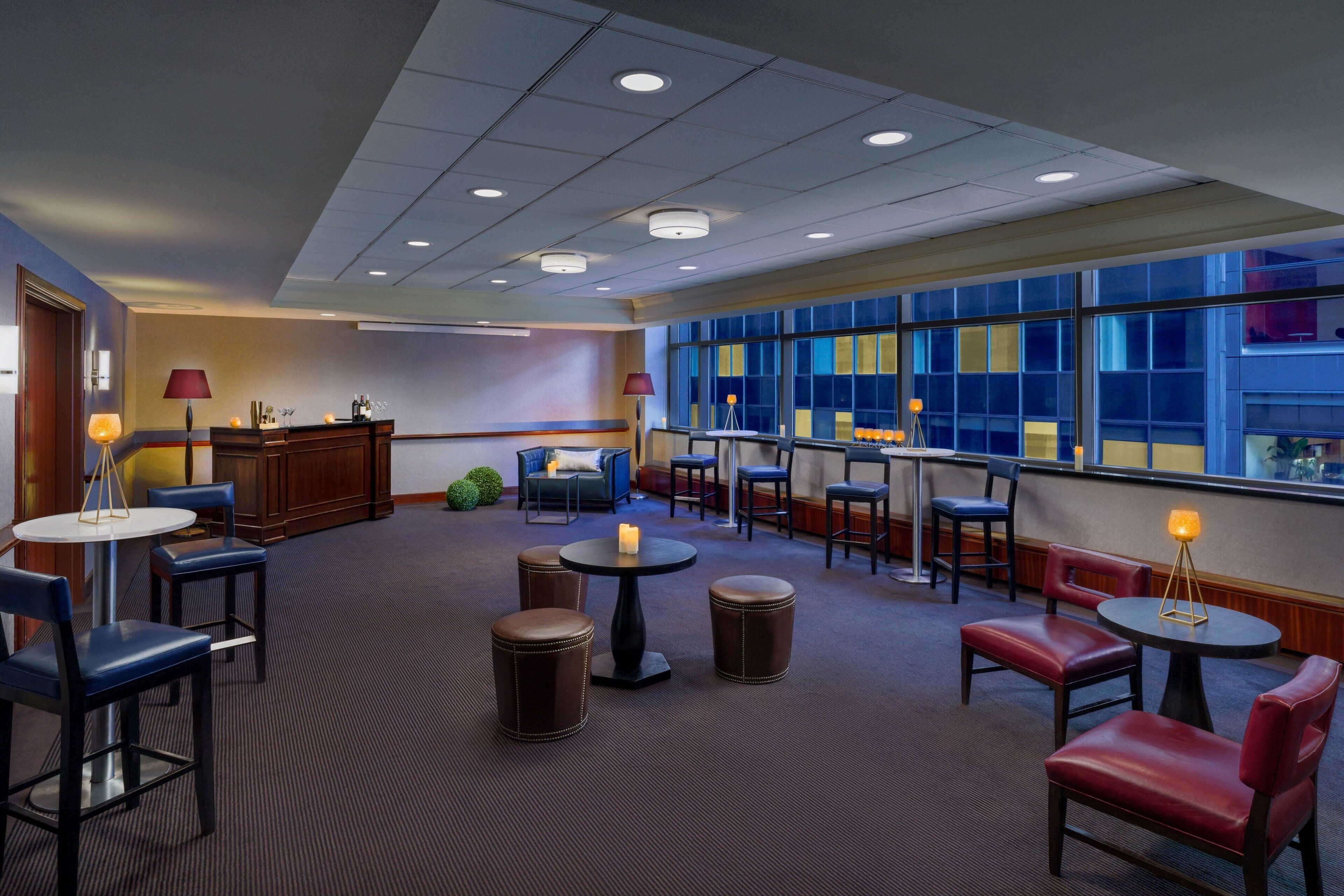 A hotel lobby with round tables, leather chairs, and a large window with a view.