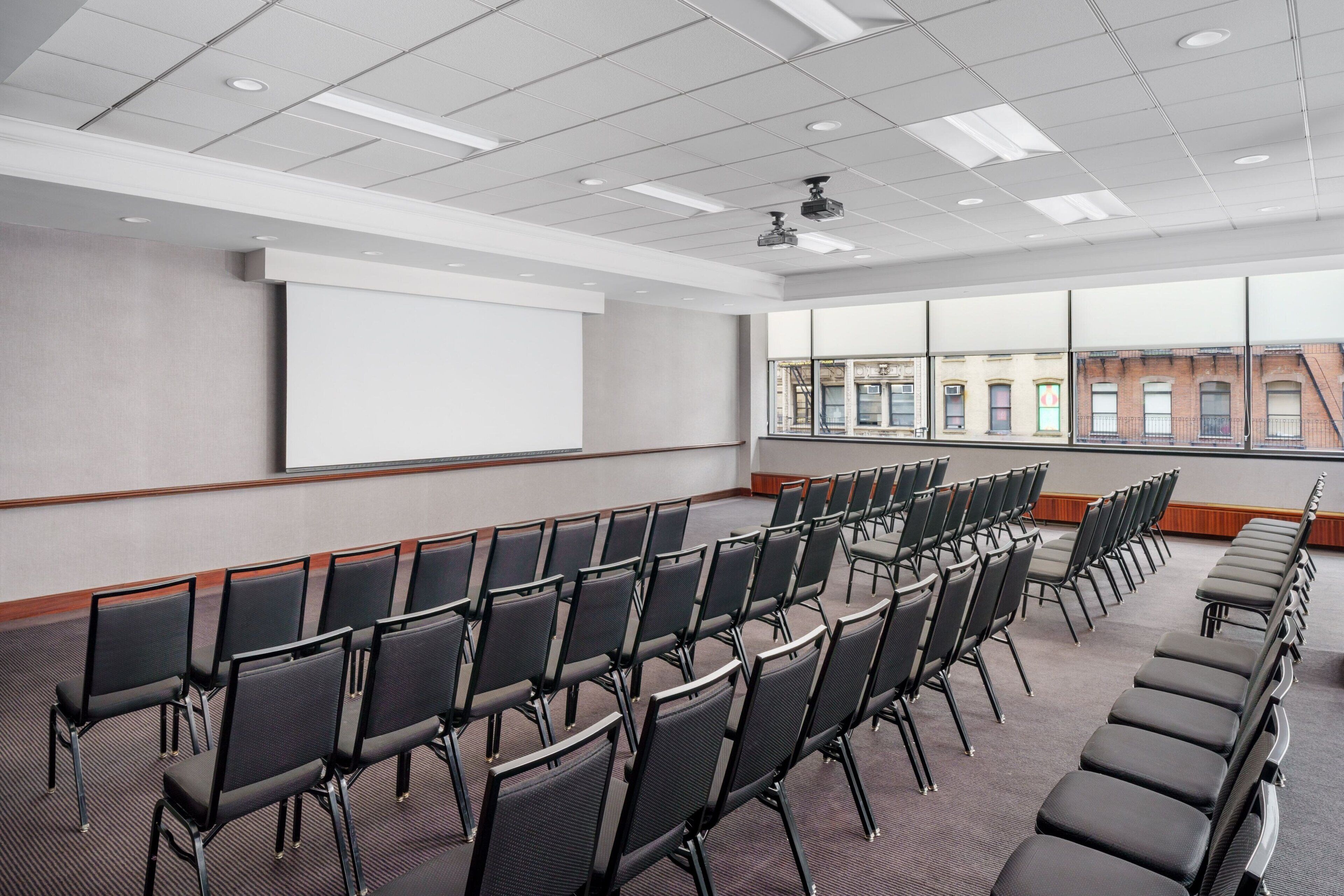 A conference room with rows of chairs, a projector screen, and a large window with a city view.