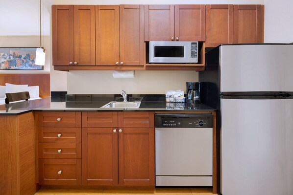 Una cocina moderna con armarios de madera, un microondas de acero inoxidable, un lavavajillas y un refrigerador.