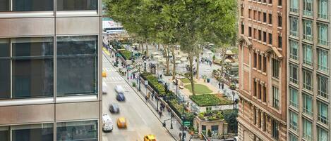 A high-rise building with a modern glass facade, a tree-lined street, and a crosswalk with pedestrians and taxis.