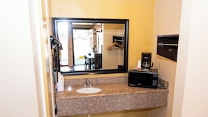 A bathroom with a granite countertop, a sink, a mirror, a coffee maker, and a hanging coat rack.