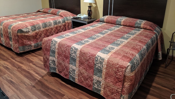 Two beds with matching quilts, a nightstand with a lamp, and a wooden floor.