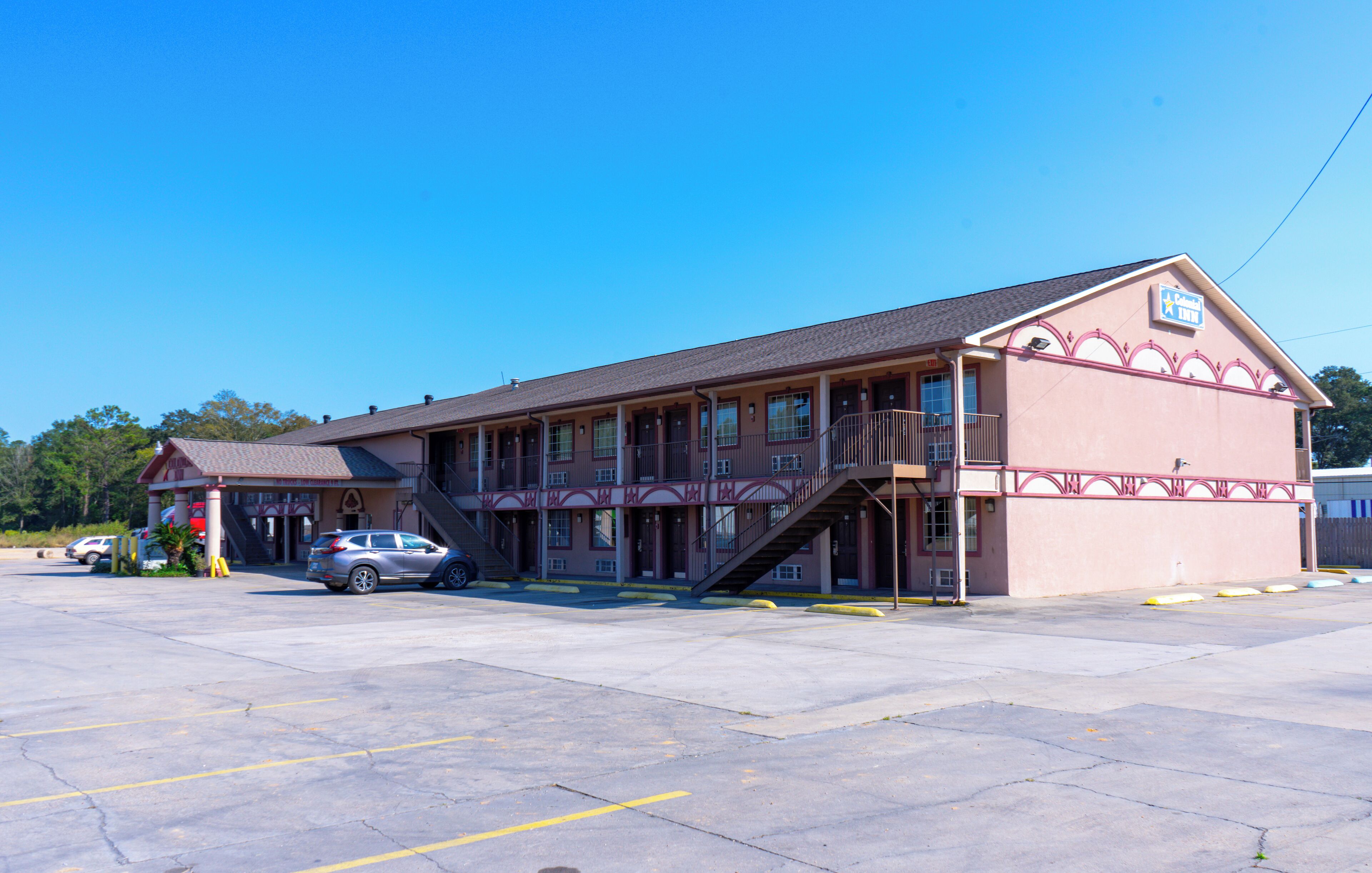 A two-story motel with a central staircase, a parking lot, and a clear blue sky.