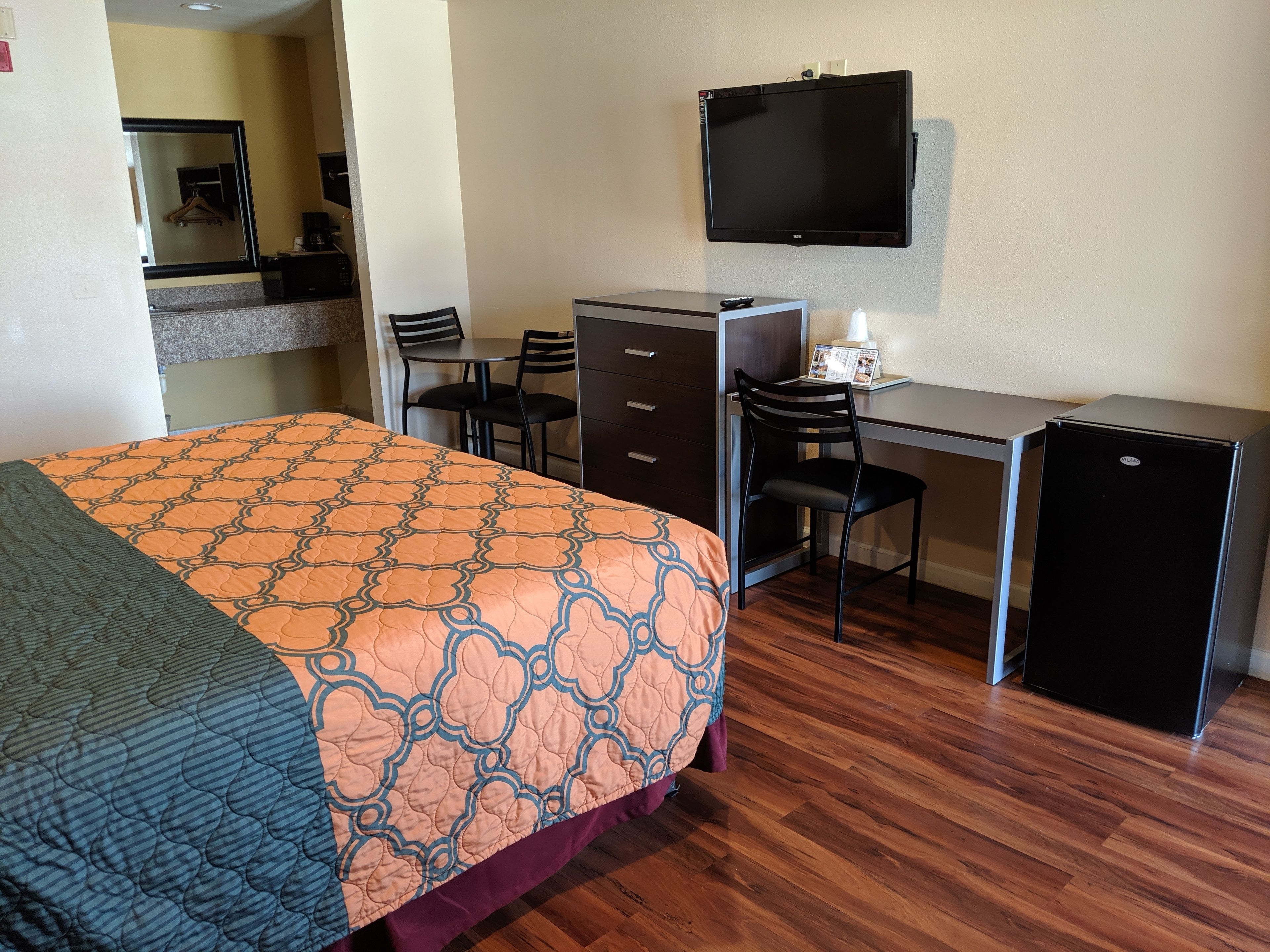 Una habitación de hotel con cama, escritorio, silla, televisor y refrigerador.